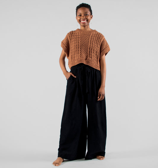 Person wearing a brown knitted top and black pants on a plain background
