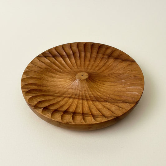 A round wooden incense burner with a carved radial pattern