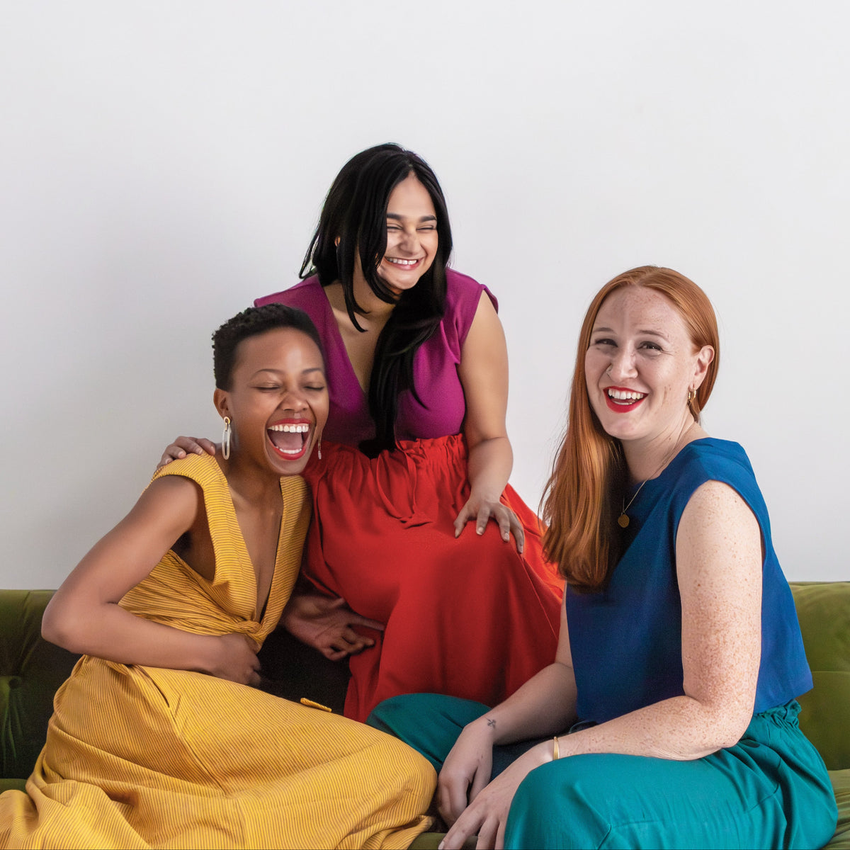 Three women sitting on a green couch against a white background