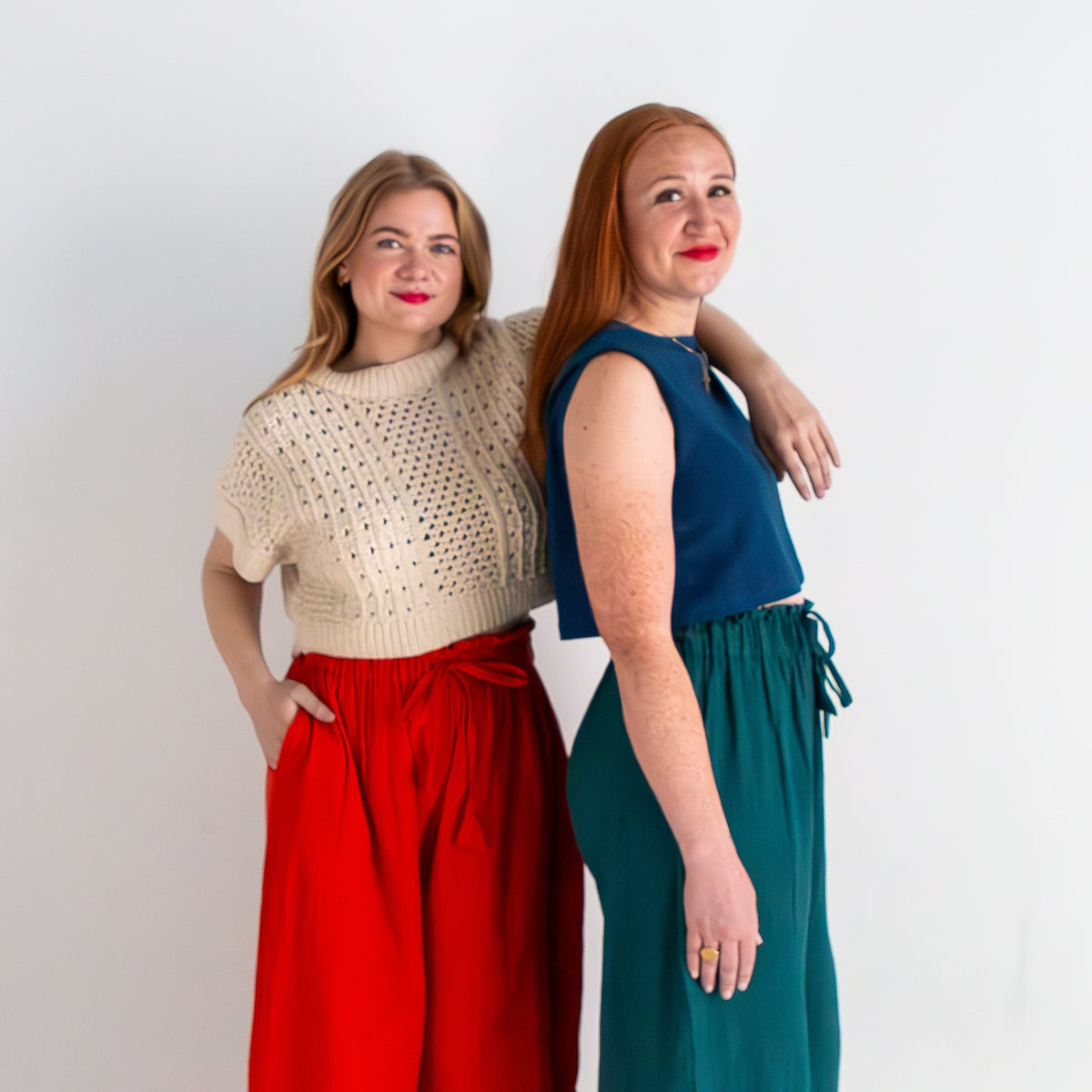 Two women standing back-to-back against a white background, wearing colorful outfits.
