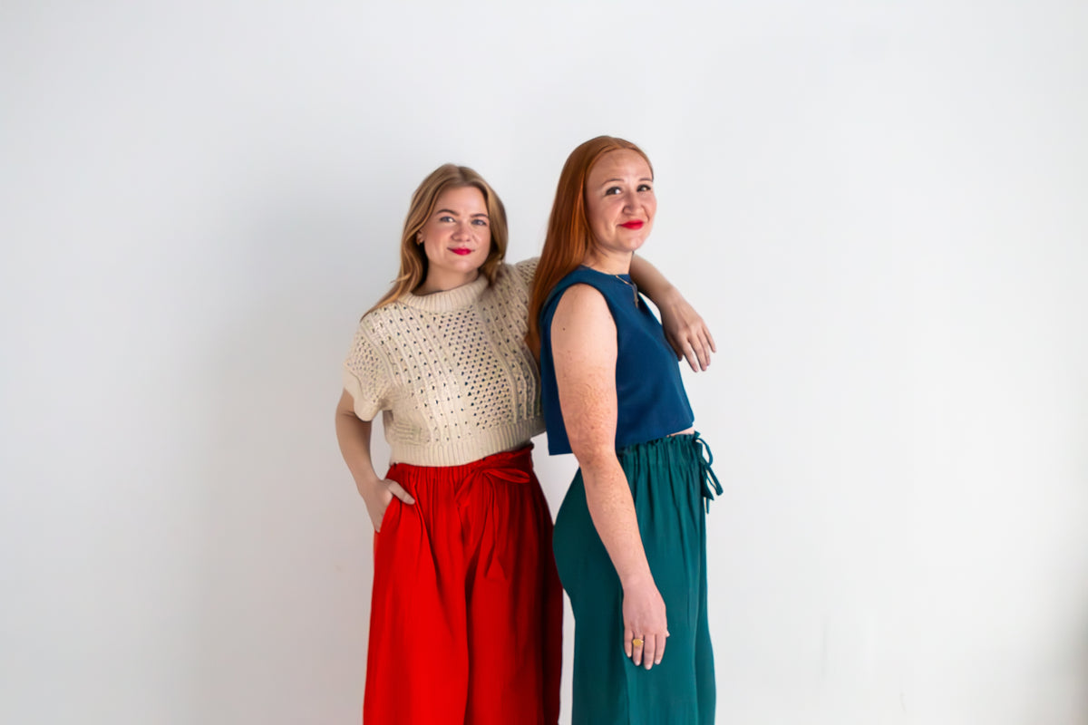 Two women standing back-to-back against a white background, wearing colorful outfits.