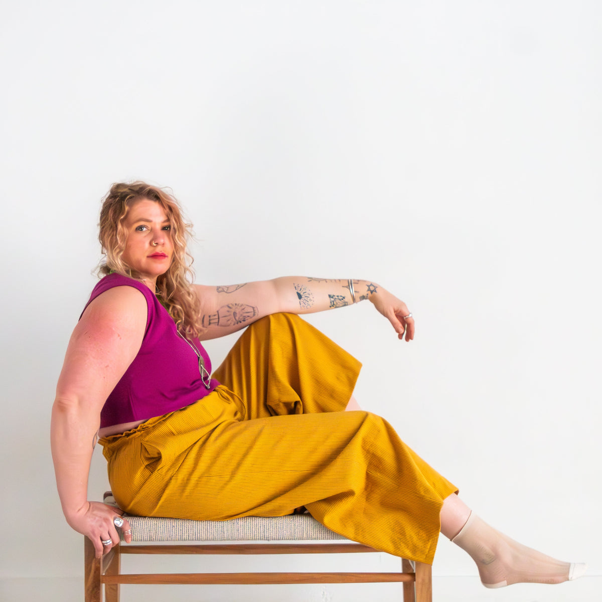 Woman sitting on a chair wearing a purple top and yellow pants against a white background