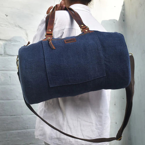 A person carrying a blue mini duffel bag with brown leather trim and a canvas shoulder strap.