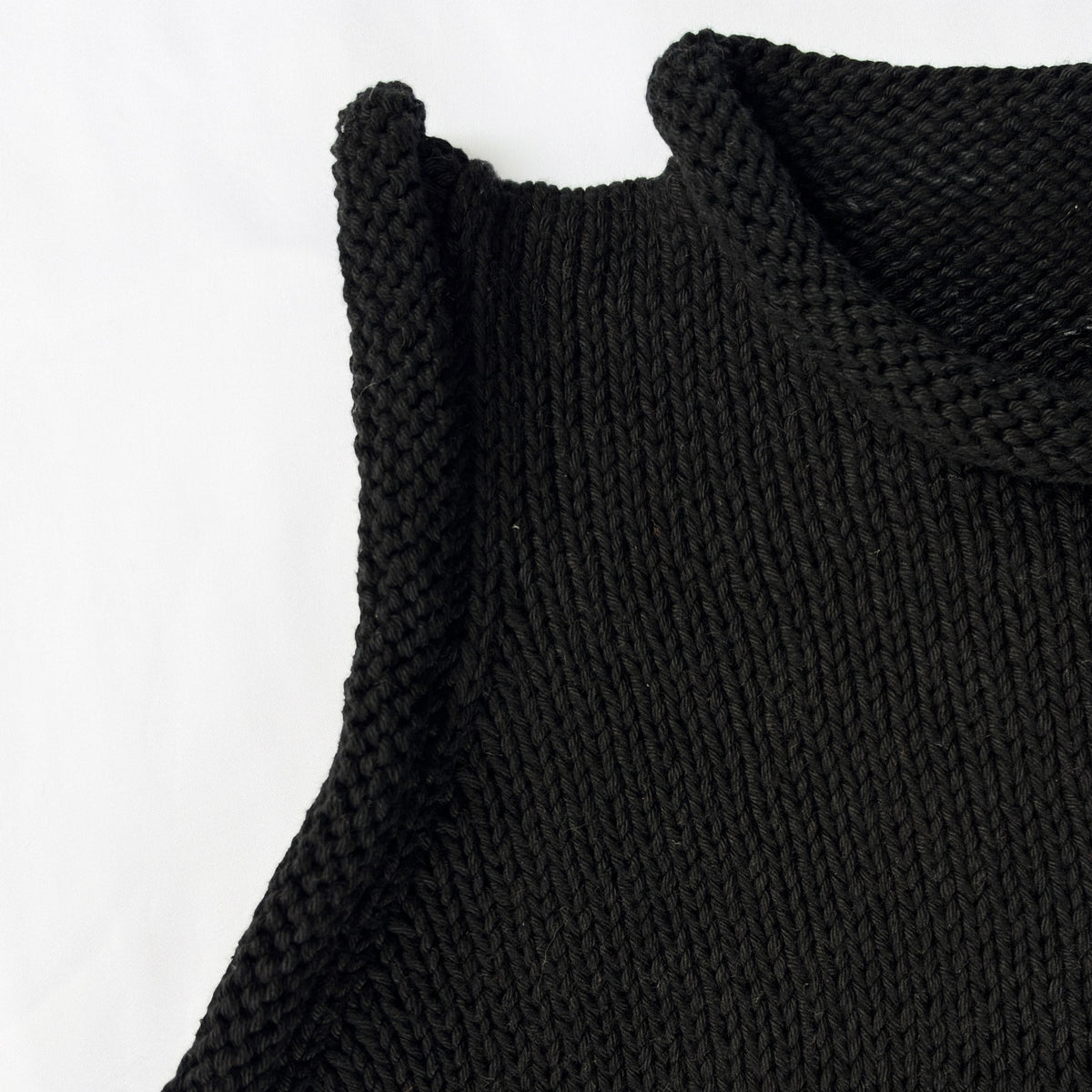 Close-up of a black knit sleeveless top with a cream-colored 'DEAR FRIEND' brand label visible inside the collar, shot against a plain white background.