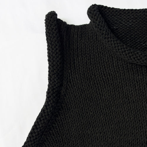 Close-up of a black knit sleeveless top with a cream-colored 'DEAR FRIEND' brand label visible inside the collar, shot against a plain white background.