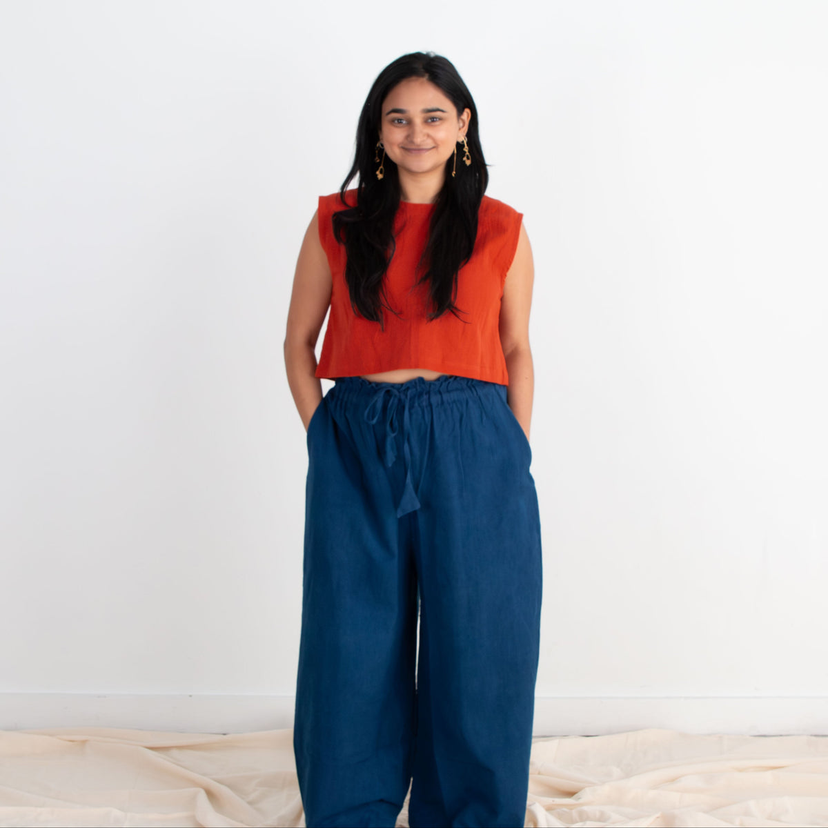 Woman wearing an orange top and blue pants standing against a white background