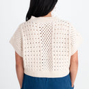 Woman wearing a beige crochet top and blue pants on a white background