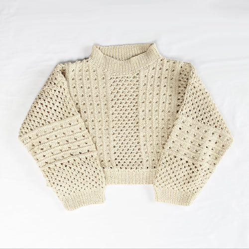 A cream-colored open-knit mock-neck sweater laid flat 