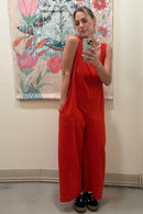 Person wearing a red jumpsuit taking a mirror selfie in front of a floral tapestry.
