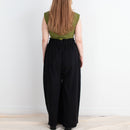 Person wearing a green top and black pants standing against a white wall.