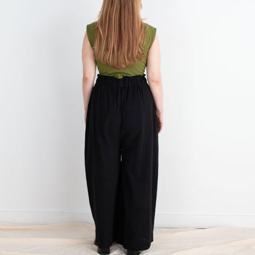 Person wearing a green top and black pants standing against a white wall.