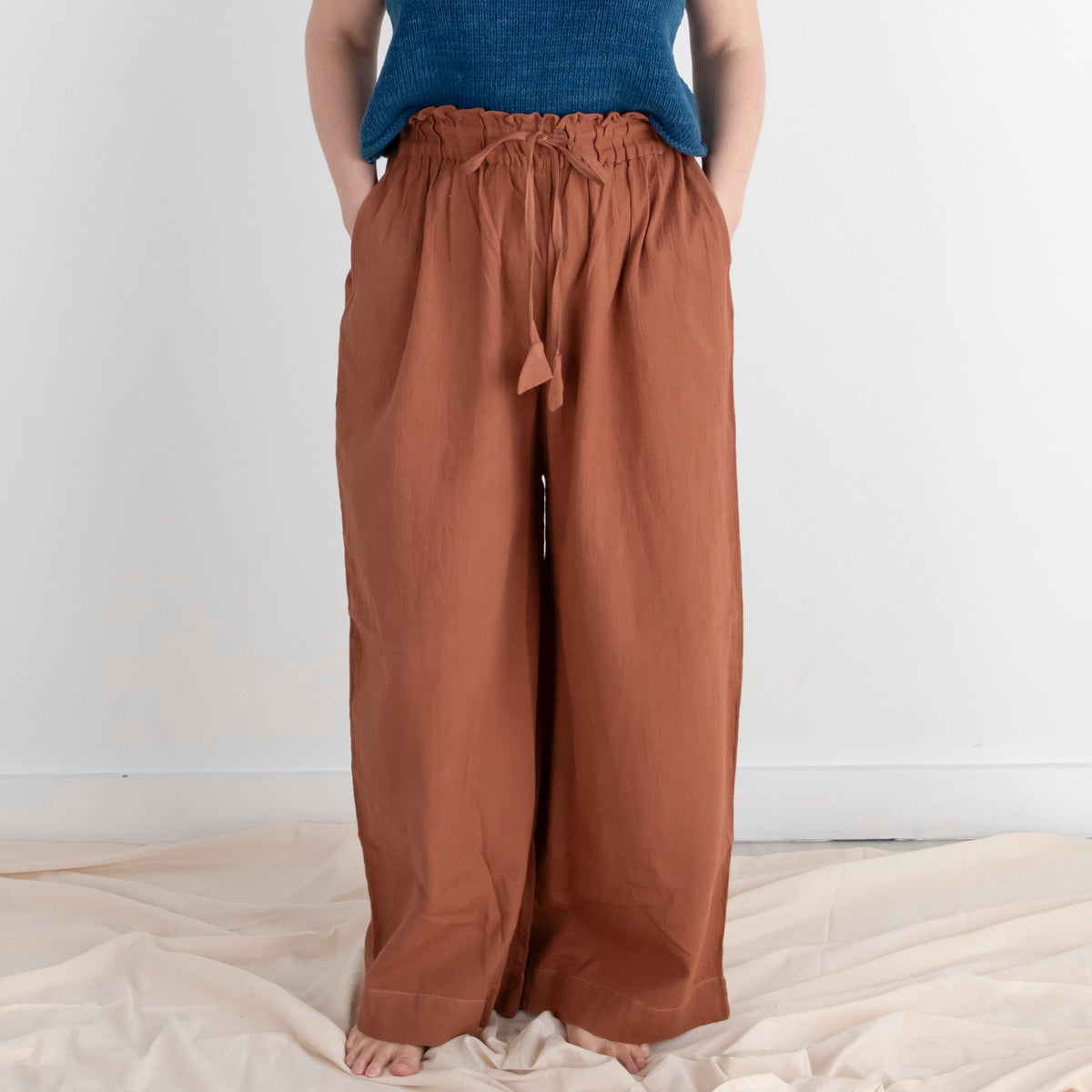 Woman wearing a blue sleeveless top and brown wide-leg pants on a white background