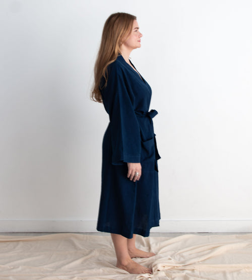 Woman wearing a navy blue robe standing against a white wall.