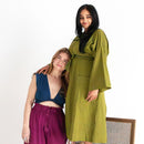 Two women wearing green and purple outfits on a white background