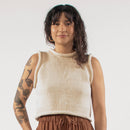 Woman standing in a studio with a white top and brown trousers