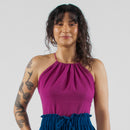 Woman wearing a purple top and blue pants standing on a white studio backdrop.