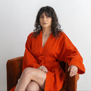 Woman wearing a red robe sitting on a chair against a white background