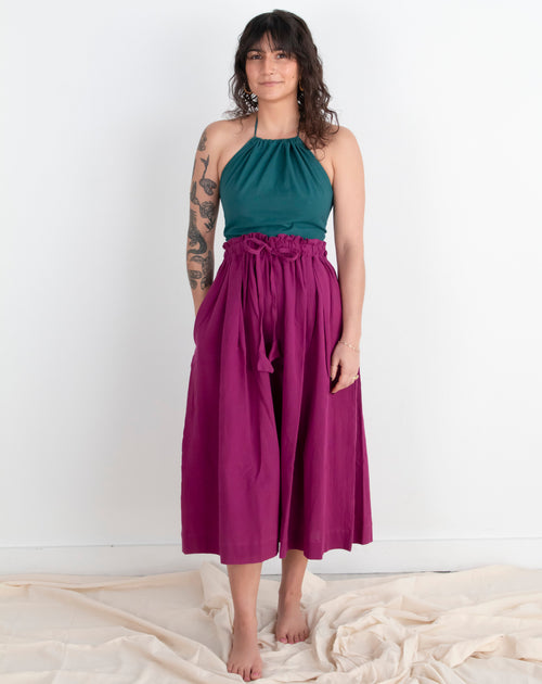 Woman wearing a teal top and magenta skirt against a white background