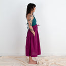 Woman wearing a teal top and magenta skirt standing against a white background