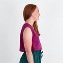 Woman wearing a purple top and teal pants against a white background