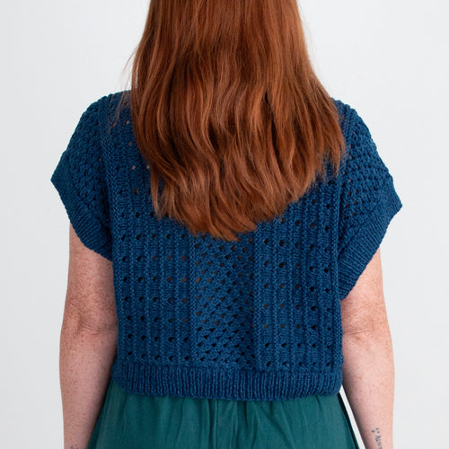 Person wearing a blue knitted top and teal pants on a white background