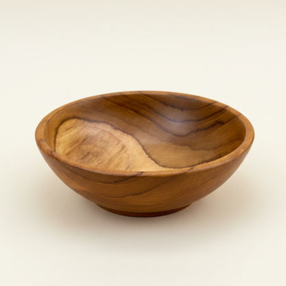 A small handcrafted wooden bowl with a polished finish, showcasing natural wood grain patterns in warm brown and tan tones