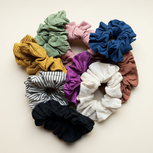 A collection of colorful handwoven cotton scrunchies in various solid colors and patterns 
