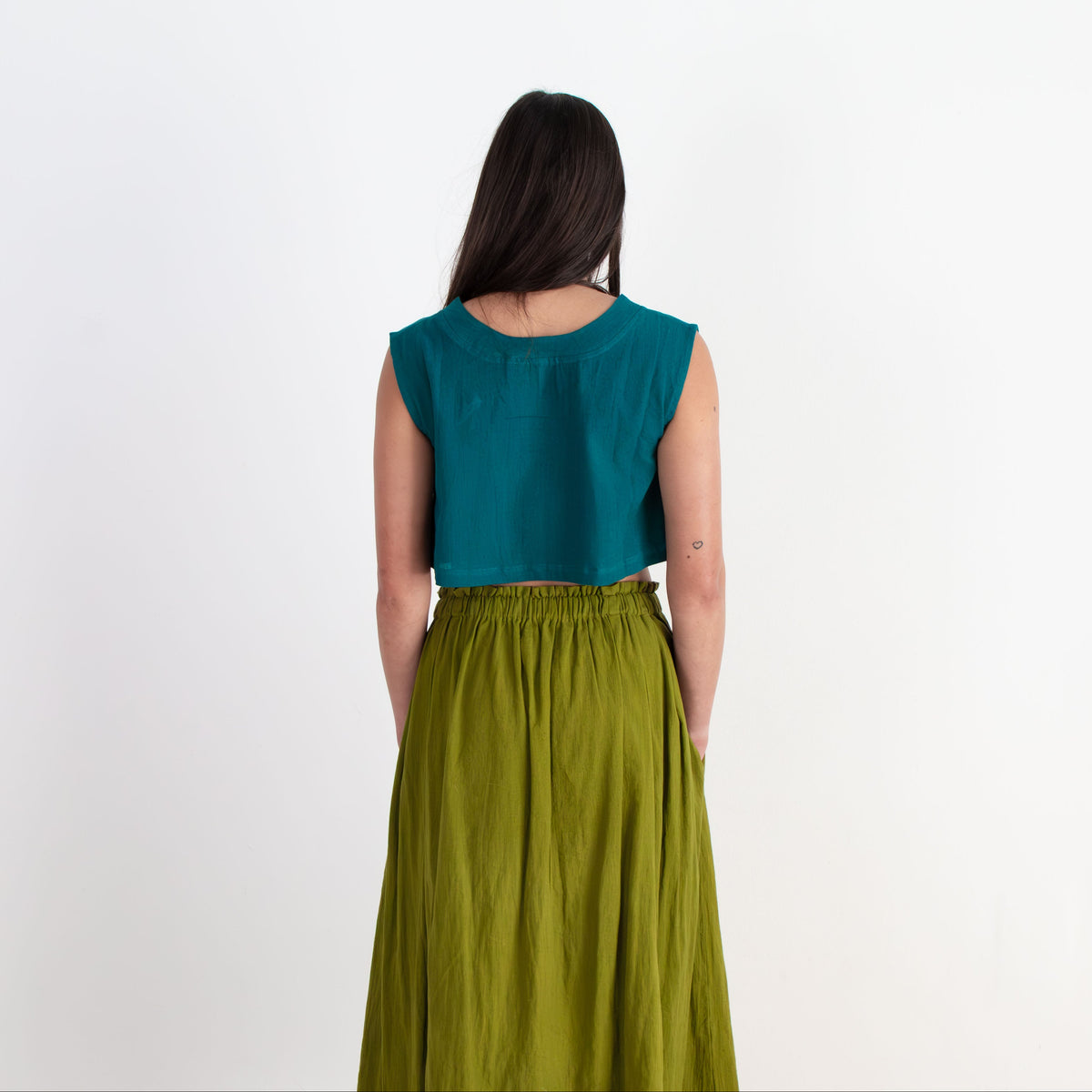 Woman wearing a teal top and green skirt on a white background