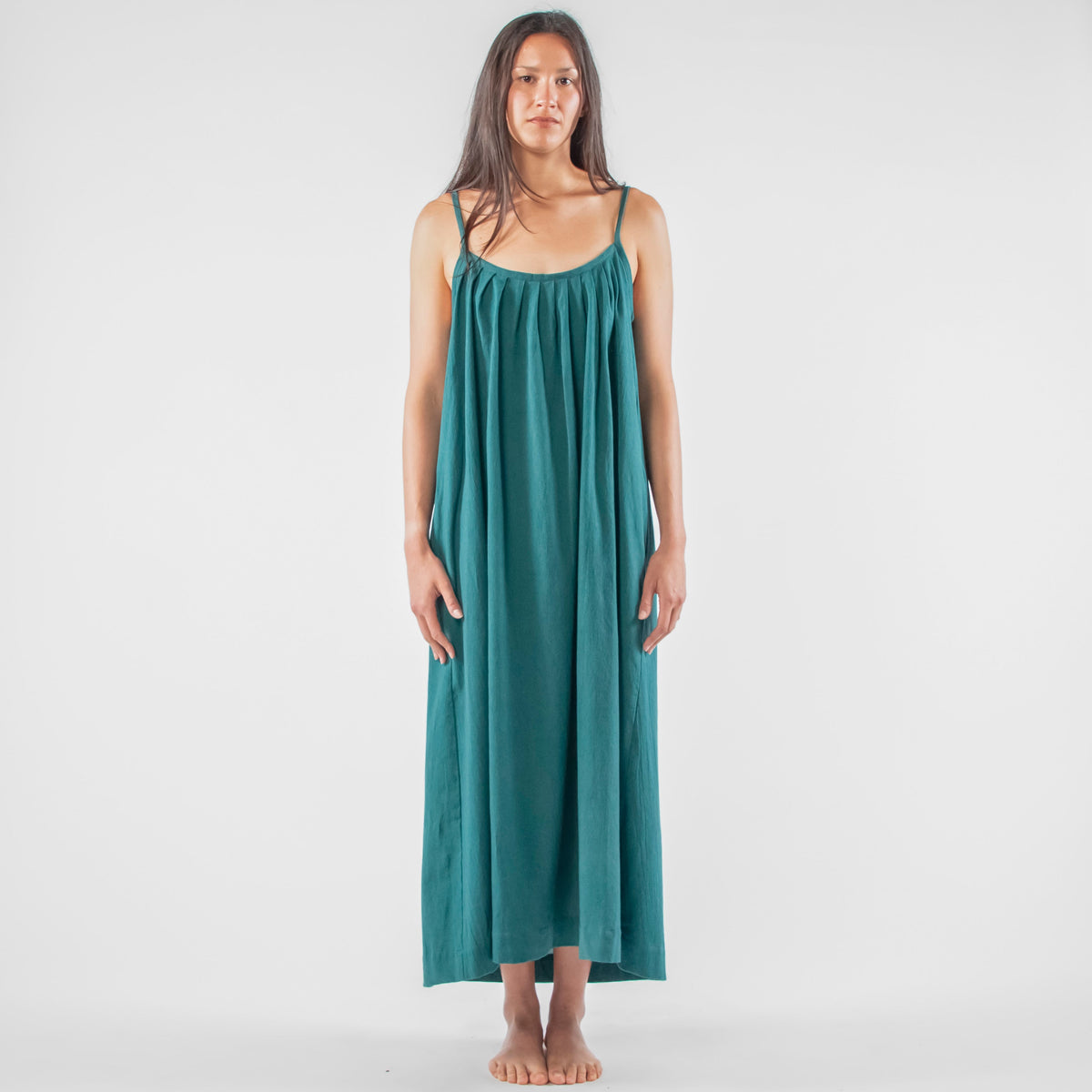 Woman wearing a teal dress standing on a white background with photography equipment around.