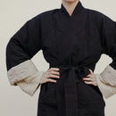 A person wearing a black quilted jacket with a matching sash belt and cream-colored sleeve cuffs.